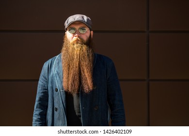 Bearded Man. Portrait Of An Serious Caucasian Adult Man With A Very Long Beard In A Cap And Sunglasses On A Sunny Day Outside.