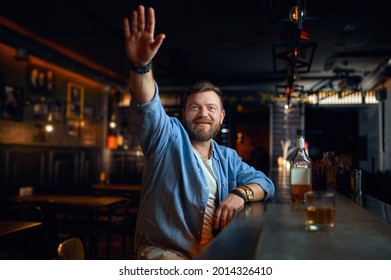 Bearded Man With Raised Hand Sitting In Bar