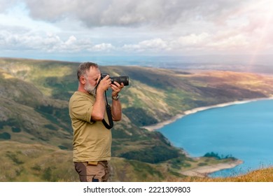 Bearded Man reaching the destination and on the top of mountain at sunset on autumn day and taking photos of amazing landscape. Travel Lifestyle concept. The national park Lake District in England