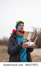 Bearded man with remote controller, dressed as a mad pilot, carefully controls the flying drone. Spring day on the coast.