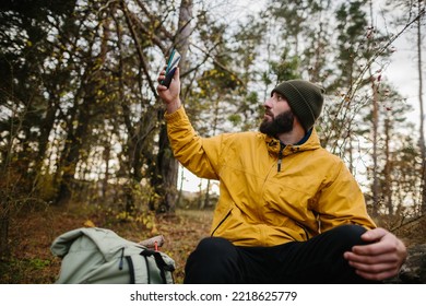 A bearded man rests on a fallen tree in the middle of the forest. A man uses a mobile phone to search GPS. - Powered by Shutterstock