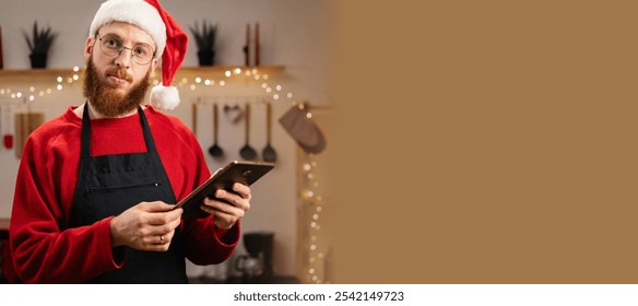 Bearded Man in Santa hat making dough while watching online cooking course via tablet in decorated kitchen on Christmas holiday. Banner. Copy space - Powered by Shutterstock