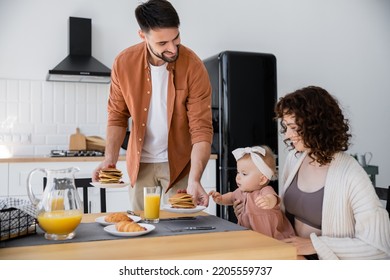 Bearded Man Serving Pancakes To Happy Wife With Infant Daughter During Breakfast