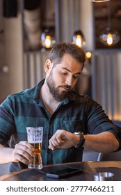 Bearded man sitting in a cafe and checking time on his watch