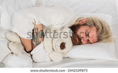 Bearded man sleeping at bedroom and hugging soft teddy bear. Handsome male sleeping with plush teddybear relaxing in bed. Good night. Sleepy man in pajamas sleeping in bed at home with teddy bear toy.