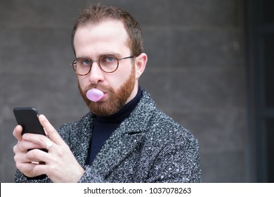 Bearded Man With Smartphone Blowing A Bubble With Bubblegum