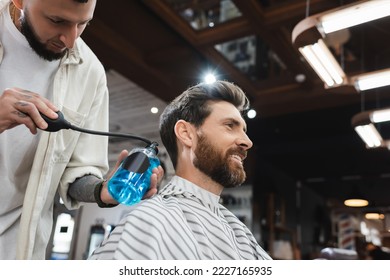 bearded man smiling near barber spraying perfume on his hair