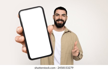 Bearded man is standing, holding a smart phone with white blank screen in his hand. The phone appears to be in use, as he is looking at the screen intently. - Powered by Shutterstock