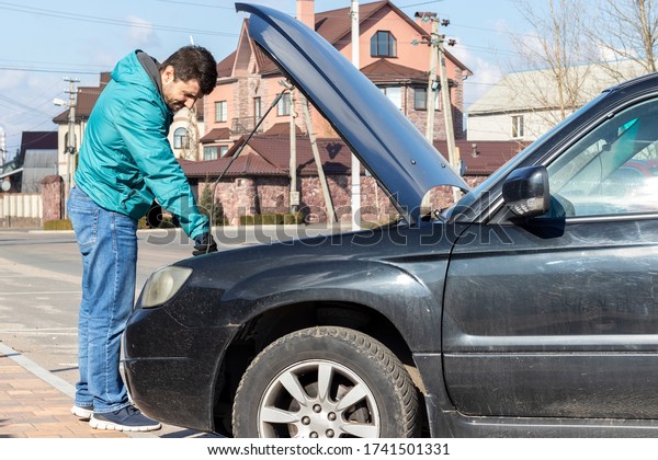 A bearded man\
standing next to the open hood of a black car during the repair\
process on a sunny day. Oil or antifreeze filling, machine self\
service and diagnostic