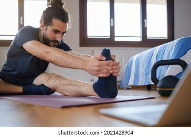 Bearded Man Stretching On The Floor At Home During An Online Exercise Class.