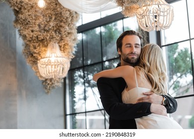 Bearded Man In Suit Hugging Blonde Girlfriend In Restaurant