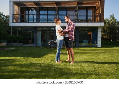 Bearded man talking with charming Caucasian female in front of the modern house - Shutterstock ID 2068153700