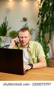 Bearded Man Talking Speaking On Phone Using Laptop. Male Employee Have Smartphone Call Cellphone With Client Or Business Partner.