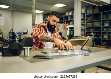 Bearded man technician testing computer part in electronics workshop. Engineer disassembling parts of a hardware component in a repair shop.