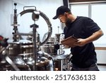 Bearded man, technologist checking brewing tools, making notes, demonstrating expertise needed to crafting beer. Concept of beer, brewery, manufacture, quality control