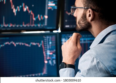 Bearded man trader wearing eyeglasses sitting at desk at office monitoring stock market looking at monitors analyzing candle bar price flow touching chin concerned trading concept close-up - Shutterstock ID 1803009610
