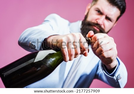 Bearded man trying to open bottle of wine with hands. Brutal handsome male with champagne.