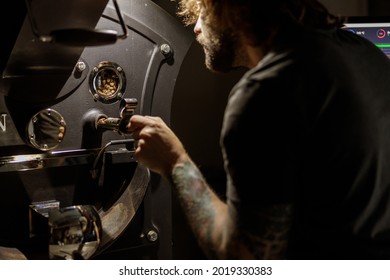Bearded man using coffee roasting machine at factory