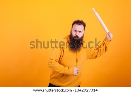 Bearded man using paddle as if was a baseball bat over yellow background. Agressive expression.