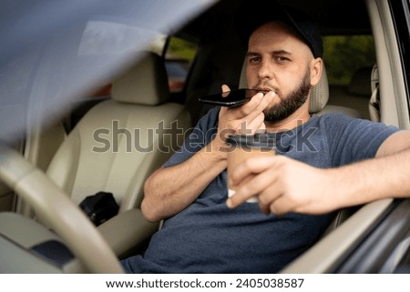 Bearded man using smartphone and talking on the speaker while driving car. Male driver talking on in-car speakerphone. Copy space