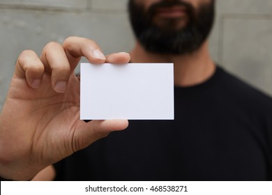 Bearded Man Wearing Casual Black Tshirt Showing Blank White Business Card.Blurred Background Ready Corporate Private Information.Horizontal Mockup