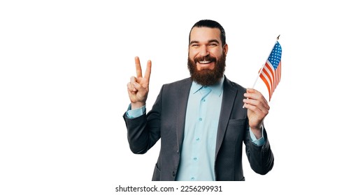 Bearded man wearing shirt and jacket is holding USA flag and finger for peace over white background. - Powered by Shutterstock