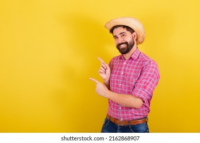 Bearded man wearing typical clothes for party Junina. showing with fingers, to the side, negative advertising and text space. For the Arraia Party - Shutterstock ID 2162868907