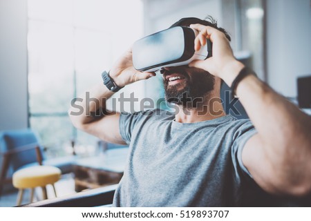 Bearded man wearing virtual reality goggles in modern coworking studio. Smartphone using with VR headset. Horizontal, blurred