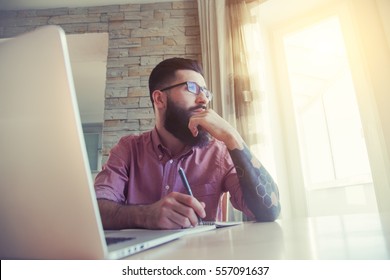 Bearded Man Working With Laptop And Writing With Pen In Notebook