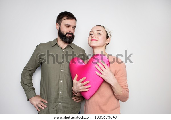 Bearded man and young\
girl play with red soft toy heart. Couple in love tears big heart\
on white background