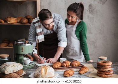 Bearded man and young woman writing a recipe of bread standing near table - Powered by Shutterstock