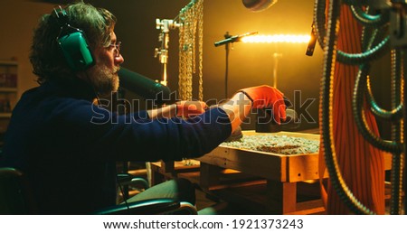 Bearded mature man on wheelchair imitating steps of robot and metal rattle while recording soundtrack for 3D movie