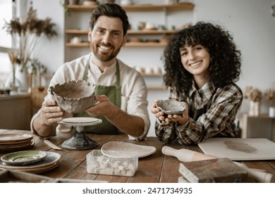 Bearded mature man and woman sculpting pottery in studio. Male sculpts vase while female sculpts bowl. Creative activity, teamwork and artistic craftsmanship. - Powered by Shutterstock