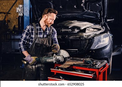 Bearded mechanic cuts steel car part with an angle grinder in a garage. - Powered by Shutterstock