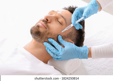 Bearded middle aged man getting beauty injection in salon. Cosmetologist hands in blue rubber gloves doing anti-aging procedure for handsome man in clinic. Face care, male cosmetology concept