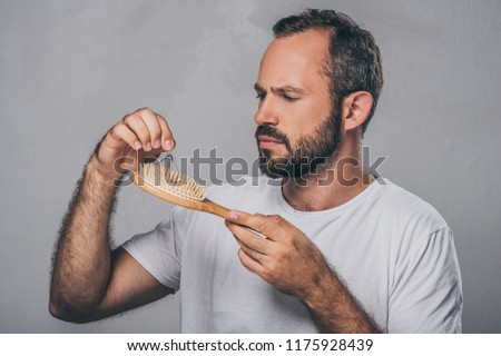 bearded middle aged man holding hairbrush, hair loss concept