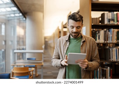 Bearded middle aged man is using digital tablet, looking for e book. Attractive latin student in library, concept of online education, studying at university, college