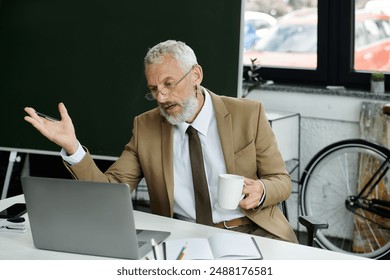 A bearded, middle-aged man, dressed in a suit and tie, sits at a desk in front of a laptop, gesticulating while teaching a class online, lgbtq teacher