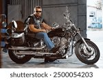 Bearded motorcyclist in black leather clothing with his motorbike