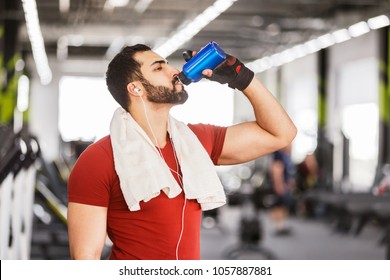 Bearded muscular man wears red t-shirt drink water from blue bottle in the gym