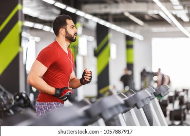 Bearded muscular man wears red t-shirt does cardio running workout in the gym
