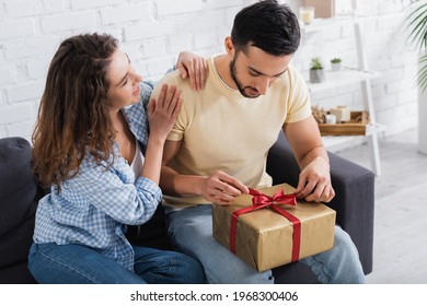 Bearded Muslim Man Pulling Ribbon On Wrapped Present Near Smiling Girlfriend