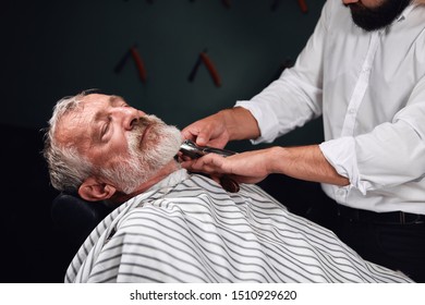 Bearded Old Man Lying On The Chair With Closed Eyes Getting Haircut. Close Up Photo