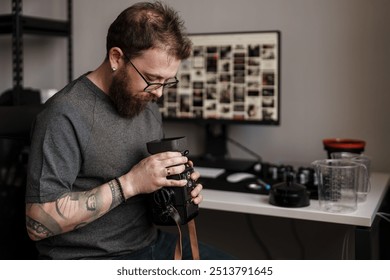 Bearded photographer focused on examining a camera lens with photography gear in the background in a well-organized home office. - Powered by Shutterstock