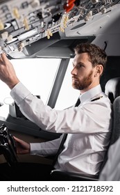 Bearded Pilot Reaching Overhead Panel While Using Yoke In Airplane Simulator