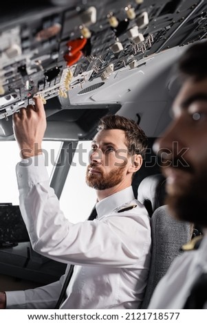 bearded pilot reaching overhead panel near co-pilot in airplane simulator