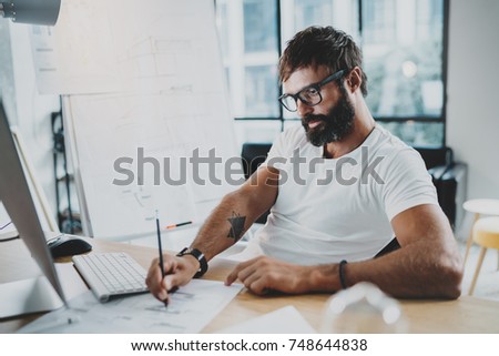 Bearded professional architect wearing eye glasses working at modern loft studio-office with desktop computer.Blurred background. Horizontal