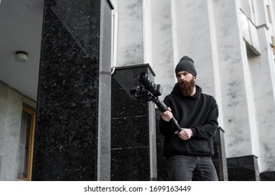 Bearded Professional Videograf in schwarz-weißer, professioneller Kamera auf 3-achsigem Gimbal-Stabilisator. Filmemacher machen ein tolles Video mit einer professionellen Kinokamera. Kameramann.