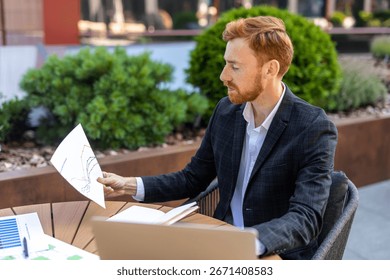 Bearded red-haired worker analyzing data at outdoor table