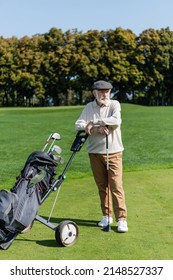 Bearded Senior Man In Flat Cap Standing Near Golf Cart